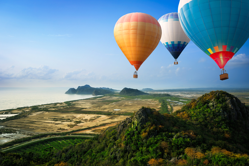 Image of three hot air balloons floating near a large hill.