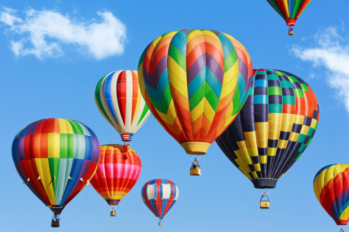 Image of six hot air balloons against a blue sky.